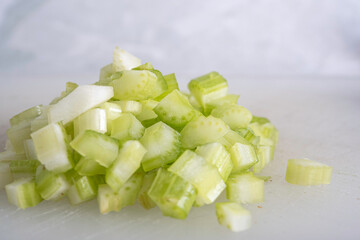 Green Celery Being Sliced on White Cutting Board With Chef's Knif and Wood Stand