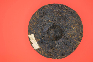 Round flat disc of puer tea isolated on a red background. Pressed Chinese fermented Pu-erh tea. Minimalism. Copy space. 