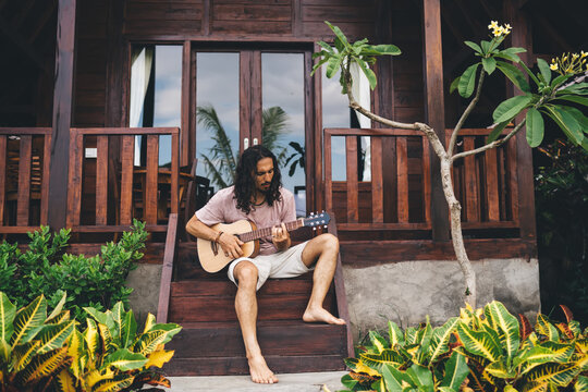 Concentrated man playing guitar on steps of house