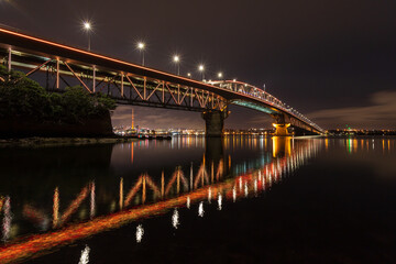 The Auckland Harbour Bridge, Auckland, New Zealand, at night, reflected in the waters of Waitemata...