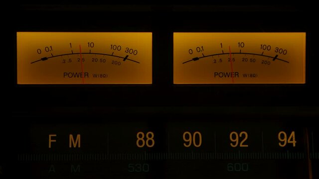 Yellow controls dashboard on an old analog radio. Extreme close up of indicator needle movement reading level going up and down on vintage electronic sound audio device. Close up. Slow motion.