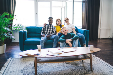 Positive multiethnic partners resting on sofa after work in apartment