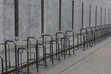 Long row of empty bike racks next to sidewalk near closed public school with bleak grey conrete wall during winter christmas school holidays
