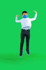 Full length photo of preschool boy in a medical mask that bounces on a green background. Kid pandemic concept