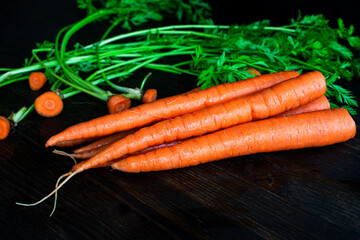 Organic Carrots on a Cutting Board: Removing the tops from carrots on a dark wood cutting board