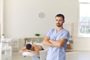 Smiling confident man masseur standing over relaxing man patient - obrazy, fototapety, plakaty