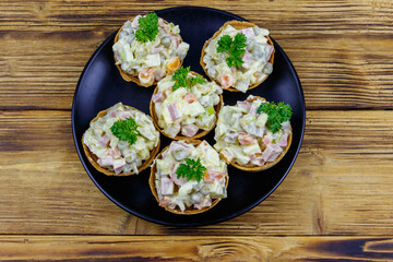 Traditional Russian festive salad Olivier in tartlets on wooden table