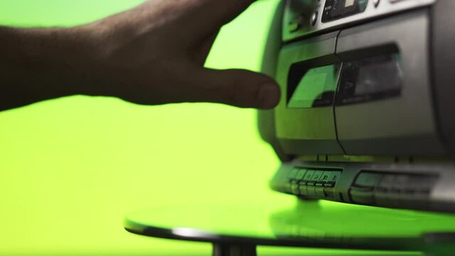 A man inserts an audio cassette into a tape recorder on a green background. Hand close up. Retro technique. Previous generation of audio systems