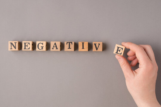 Pessimism concept. Close up top view photo of female hand putting wooden cubes with negative word on gray table