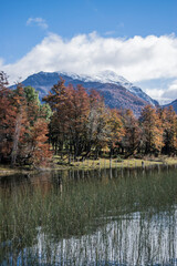 sunset between the clouds in a lake between two mountains with snow inside a colorful forest during autumn in bariloche, argentina