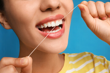 Young woman flossing her teeth on blue background, closeup. Cosmetic dentistry