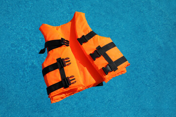 Bright orange life jacket floating in swimming pool, top view