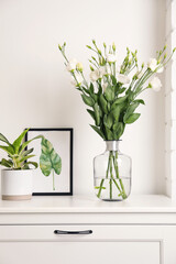 Decorative vase with flowers and houseplant on commode indoors