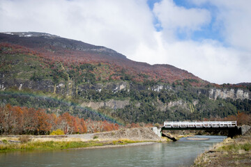 Fototapeta premium old wooden bridge over the river in a mountainous landscape with the rainbow in patagonia argentina