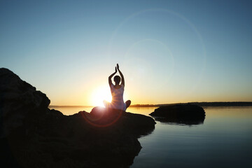 Woman practicing yoga near river on sunset. Healing concept