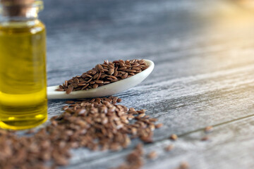 Brown flaxseeds, jar with linseeds oil and spoon on gray table.