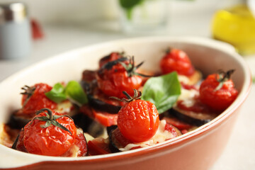 Baked eggplant with tomatoes, cheese and basil in dishware on table, closeup