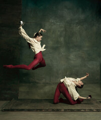 Attacking. Two young female ballet dancers like duelists with swords on dark green background. Caucasian models dancing together. Ballet and contemporary choreography concept. Creative art photo.