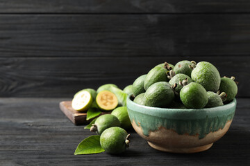 Fresh green feijoa fruits on black wooden table, space for text