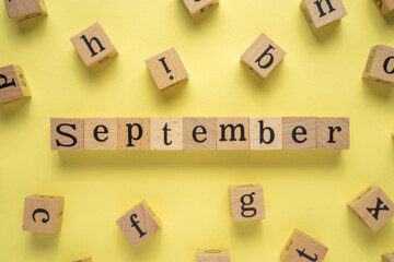 Text SEPTEMBER on wooden cubes with a yellow background. Flat lay view concept.