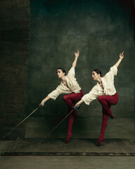 Line. Two young female ballet dancers like duelists with swords on dark green background. Caucasian models dancing together. Ballet and contemporary choreography concept. Creative art photo.