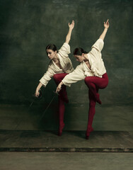 Line. Two young female ballet dancers like duelists with swords on dark green background. Caucasian models dancing together. Ballet and contemporary choreography concept. Creative art photo.