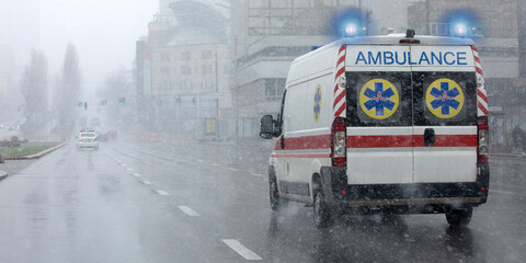 Ambulance with flashing lights moves down the street in bad weather. © CreativeSuburb
