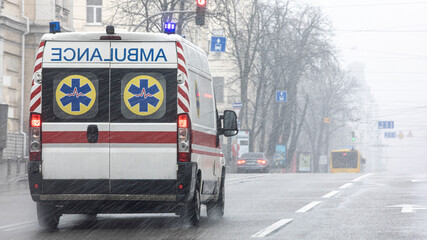 Ambulance with flashing lights moves down the street in bad weather. © CreativeSuburb