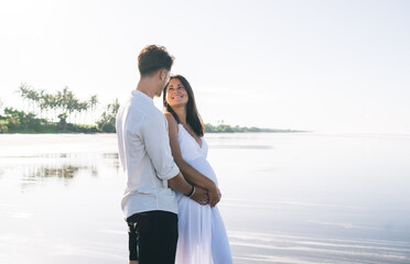 Loving husband embracing pregnant wife on seashore