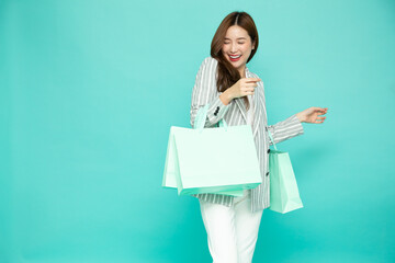 Young Asian woman holding light green shopping bags isolated on green background