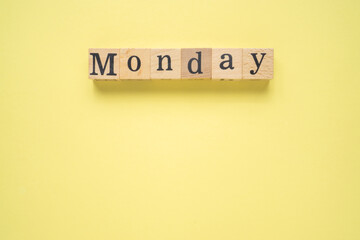 Text MONDAY on wooden cubes with a copy space on yellow background. Flat lay view concept.