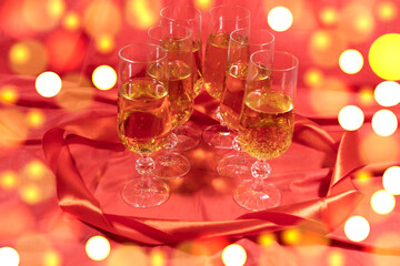 Against the background of blurry shiny lights оn a red background are six glasses of champagne framed by a red ribbon.