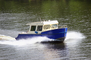 Fast gliding 32 ft outboard motor boat with reverse tilt of the windscreen front side view on green trees on far shore background at Sunny summer day, active boating tourism recreation on river