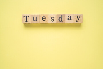 Text TUESDAY on wooden cubes with a copy space on yellow background. Flat lay view concept.