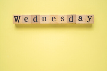 Text WEDNESDAY on wooden cubes with a copy space on yellow background. Flat lay view concept.