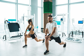 Fototapeta na wymiar Focused sportspeople doing lunges near modern equipment in gym