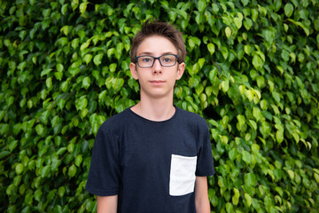 Teen boy 13 years old posing in summer park with ficus trees in summer Spain