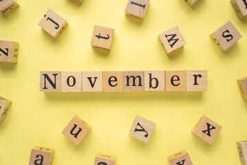 Text NOVEMBER on wooden cubes with a yellow background. Flat lay view concept.