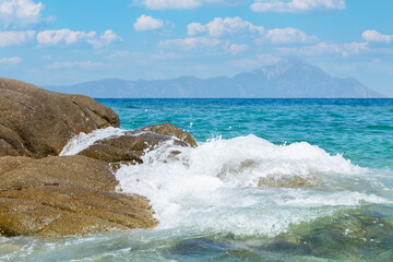 Aegean Sea Blue water waves Crashing on Rocks of Sithonia peninsula of Chalkidiki with Mount Athos on background