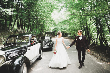 Happy newlywed couple, man and wife kissing near stylish retro car