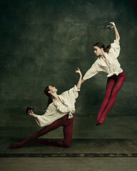 Motion. Two young female ballet dancers like duelists with swords on dark green background. Caucasian models dancing together. Ballet and contemporary choreography concept. Creative art photo.
