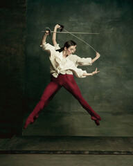 Fighting. Two young female ballet dancers like duelists with swords on dark green background. Caucasian models dancing together. Ballet and contemporary choreography concept. Creative art photo.