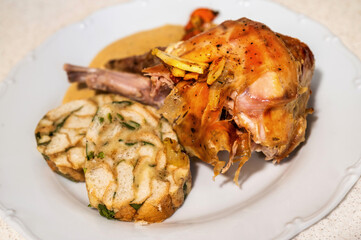 Baked rabbit leg with vegetable cream sauce and Carlsbad dumpling on white plate.