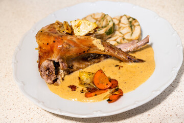 Baked rabbit leg with creamy and spicy vegetable sauce and dumpling on white plate.