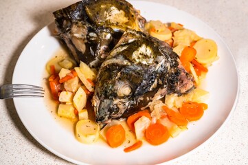 Two boiled carp fish head on plate with sliced vegetable