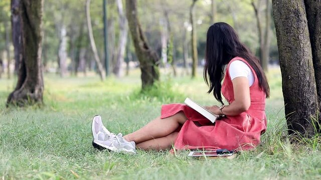 Mujer joven leyendo en el parque y  trabajando en su laptop. Concepto de chica latina trabajando en el parque