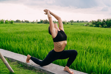 Fototapeta premium Concentrated fit girl stretching body muscles during morning pilates training near rice fields in Vietnam, calm female yogi meditating for mindfulness keeping healthy lifestyle on retreat training