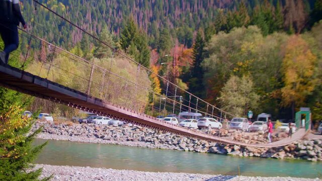 Hanging bridge over Teberda river. Dombai mountains in Caucasus. Defocsed unrecognizable people walk on bridge.