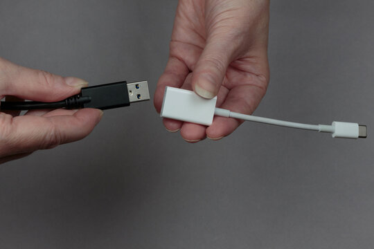 hands connecting a usb cable to a usb-c to usb adaptor on a gray background