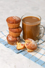 A stack of homemade muffins with filling and a Cup of coffee with milk or cocoa close up on a white table